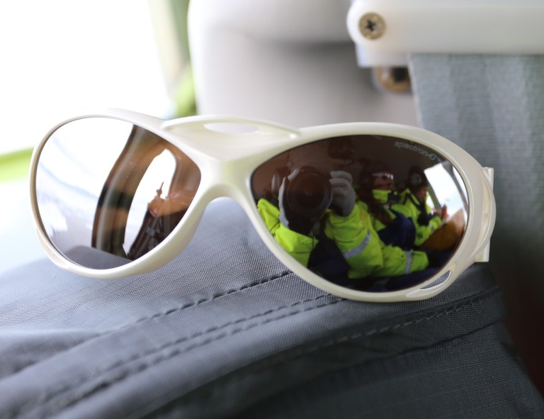 A pair of white sunglasses, with the photographer's reflection seen in one lens.