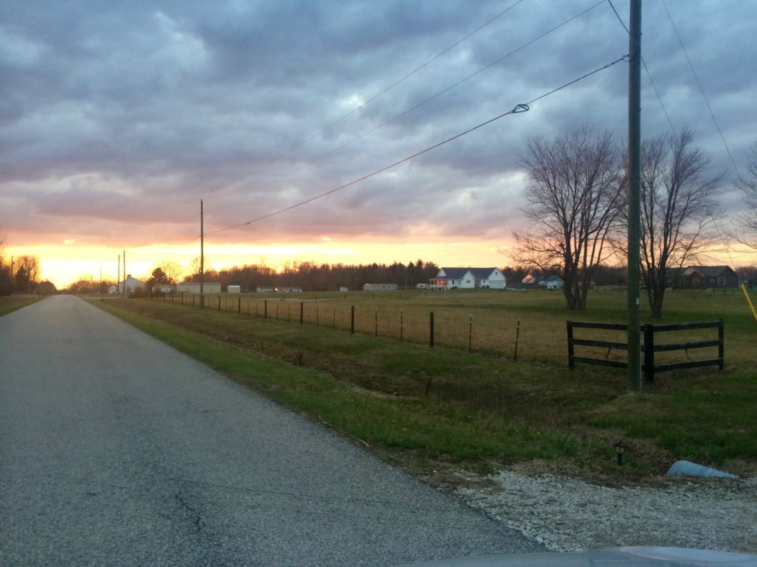 A stretch of rural road at sunset, with a small town in the distance.