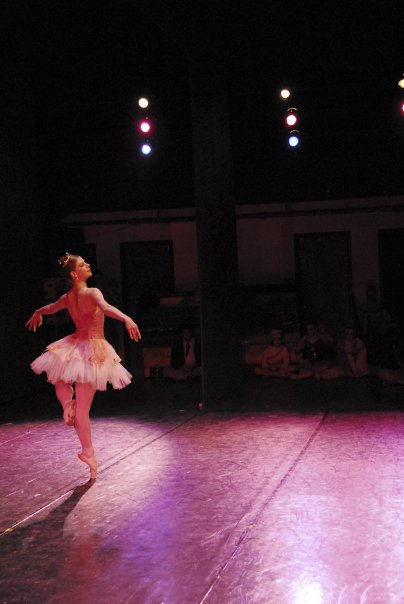 A ballet dancer in a white dress performs on a large stage.