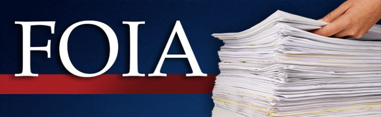 FOIA in large white letters on a red line on a blue background. On the right, a hand holds the top papers of a large stack.