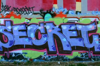 Colorful graffiti of the word secret in large purple letters on a lime, red, and white background.