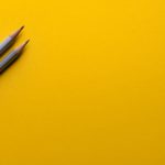 Photo of two gray pencils sitting on a yellow surface.