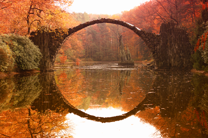 Autumn view of a bridge arching over glassy smooth water.