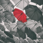 A photo of a group of umbrellas, the photo is in grayscale except for one red umbrella.