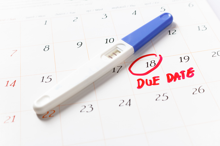 A pregnancy test, with a positive result, lying on a calendar with a day marked as DUE DATE.