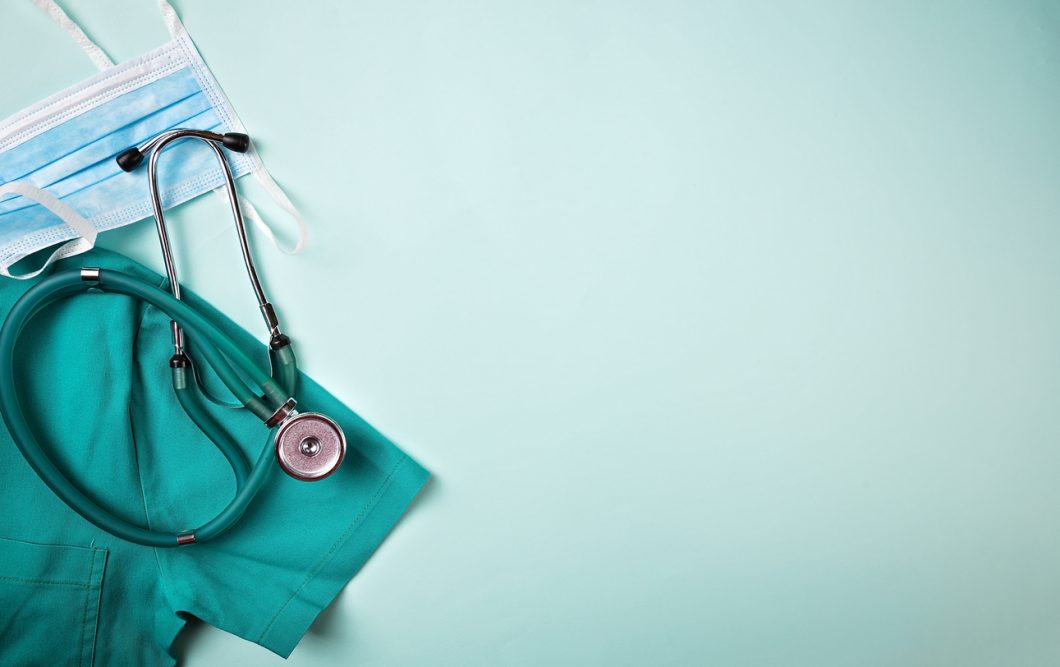 Full frame shot of face mask placed with stethoscope and medical scrubs. All are on green background