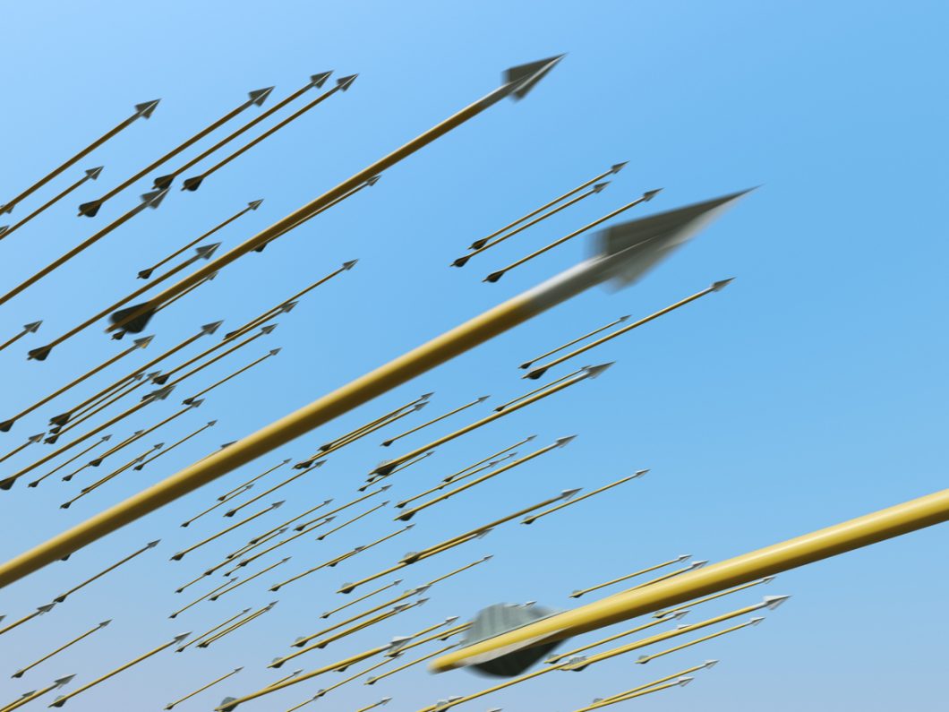 Many blurred arrows in motion flying through clear blue sky.