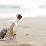 A glass bottle with a rolled-up message inside, wedged in the sand on a beach