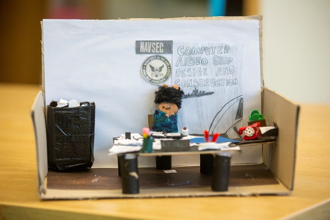 Peeps diorama showing researcher Raye Jean Jordan Montague, who created the first computer-generated rough draft of a U.S. naval ship in 1971, working in her office. The crafters reproduced a vintage rotary phone on her desk, and office plant and trash can.