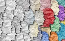 A group of faces made of tissue paper, with homogenous gray faces on the left transltioning to a diversity of colors on the right.