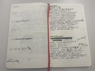An open planner sits on a nondescript surface. On the left page a few appointments and due dates are listed. On the right, there are very full "homework" and "journalism" lists.